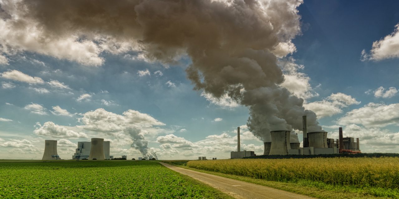 carbon markets njaga advocates Industrial power plant emitting thick smoke into the sky, situated next to green farmland, symbolizing the contrast between industrial pollution and agriculture | Landmark Judgment on Climate Change, Carbon Markets, Offset Projects, Public Participation, and Community Land Rights in Kenya | ESG and climate change lawyer in Nairobi | Njaga & Co. Advocates LLP ESG law firm